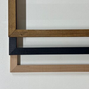 May include: Three wooden picture frames, one brown, one black, and one light wood, stacked on top of each other.