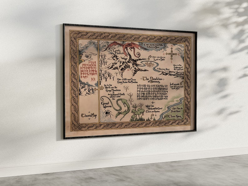 May include: Framed fantasy map with intricate illustrations and text, depicting a fictional landscape with mountains, a dragon, and a serpent. The map is in shades of brown, beige, and green, with a black frame. The map is hanging on a white wall.