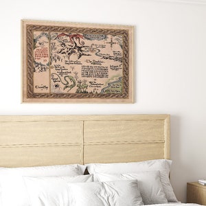 May include: A framed map with a beige background and a brown border hangs above a bed. The map features illustrations of dragons, a serpent, and text. The frame is light brown, and the map is mounted on a white wall.