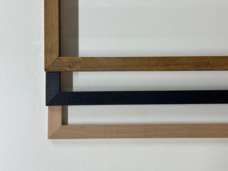 May include: Three wooden picture frames in different colors: dark brown, black, and light brown. The frames are stacked on top of each other, showcasing their various finishes and styles. The frames are displayed against a white background.