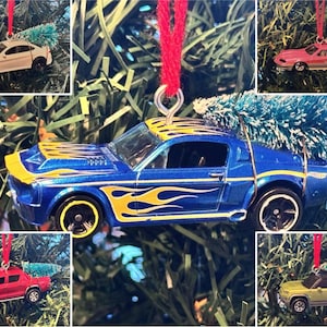 May include: A collage of miniature car ornaments in various colors, including white, pink, red, blue, and yellow. Each car has a small green Christmas tree attached to the top and is suspended by a red string, perfect for holiday decorating.