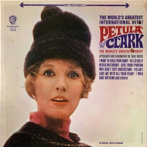 Peut inclure: Pochette d'album vintage de Petula Clark, avec le titre "The World's Greatest International Hits!". Clark porte un chapeau foncé et un col roulé rose. Le logo Warner Bros. est visible en haut à gauche.