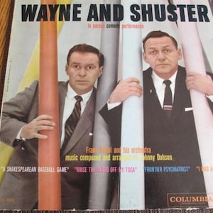 May include: Vintage vinyl record album cover featuring Wayne and Shuster, a comedy duo. The album cover has the title "WAYNE AND SHUSTER" in bold black letters. The cover includes the names of the songs and the Columbia Records logo.