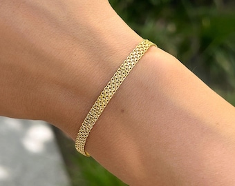 Op de afbeelding: Een gouden kettingarmband met een delicaat, ingewikkeld ontwerp. De armband is gemaakt van kleine, met elkaar verbonden vierkanten die een geweven patroon creëren.
