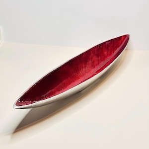 May include: A long, silver-colored decorative bowl with a vibrant red interior. The interior has a textured, ridged pattern. The bowl is elongated and has a sleek, modern design, suitable for serving or display.