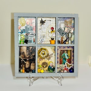 May include: A gray wooden shadow box with six compartments, each containing a collage of various objects and images. The box is propped up on a clear stand. Items include a baseball glove, a bee, and the words "BORN TO GOLF!"