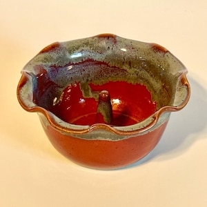May include: A red and green glazed ceramic apple baker with a fluted rim and a center post.
