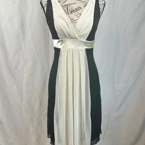May include: A black and white sleeveless dress with a white chiffon overlay and a black satin sash.