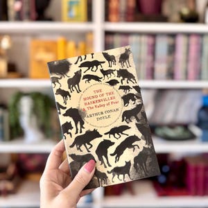 May include: A copy of "The Hound of the Baskervilles & The Valley of Fear" by Arthur Conan Doyle. The book cover features black silhouettes of dogs on a cream background. The title and author's name are in red and black.