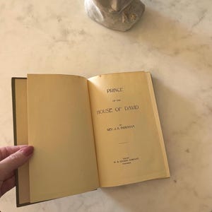 May include: An open book titled "Prince of the House of David" by Rev. J.H. Ingraham. The book's pages are yellowed with age, and the spine is dark green. The text is black, with the publisher's name at the bottom.