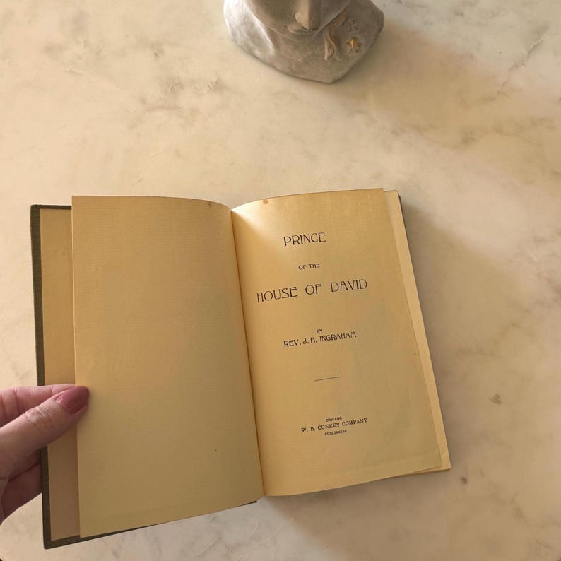 May include: An open book titled "Prince of the House of David" by Rev. J.H. Ingraham. The book's pages are yellowed with age, and the spine is dark green. The text is black, with the publisher's name at the bottom.