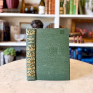 May include: A vintage hardcover book titled "The Collected Tales of A.E. Coppard." The book has a green cover with a decorative emblem and gold lettering on the spine. The book is displayed on a light-colored surface.