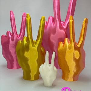 May include: Five 3D printed peace sign hand sculptures in different sizes. The largest is pink, the next two are yellow, and the smallest is white.