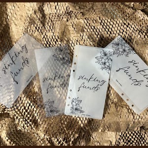 May include: Four clear plastic sheets with black floral designs and the text "sinking funds" written in cursive.