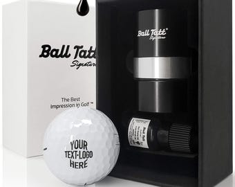 May include: A golf ball marking kit featuring a white golf ball with the text YOUR TEXT-LOGO HERE, a black and silver cylindrical stamp tool labeled Ball Tatt Signature, and a small bottle of ink, all housed in a black and white presentation box.