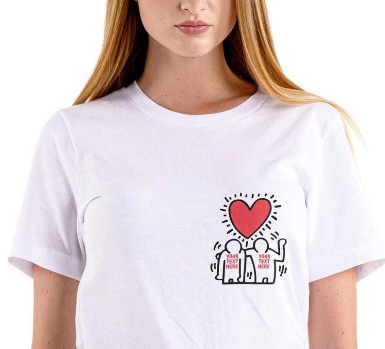 May include: White t-shirt with a black and white graphic of two figures holding a red heart. The text "YOUR TEXT HERE" is written on each figure.