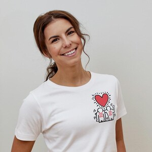 May include: White t-shirt with a red heart and two figures holding hands. The figures have the text "YOUR TEXT HERE" written on them.