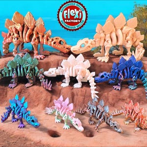 Puede incluir: Una colección de ocho esqueletos de dinosaurios articulados en varios colores, incluyendo oro, plata, azul, verde, rosa y blanco. Los esqueletos están en una variedad de posiciones dinámicas, algunos de pie y otros acostados. Los esqueletos están hechos de un material flexible y están diseñados para ser articulados, lo que permite que se coloquen de varias maneras. Los esqueletos son todos de la misma especie, un Stegosaurus, y todos son aproximadamente del mismo tamaño. Los esqueletos se muestran en una superficie marrón y arenosa.
