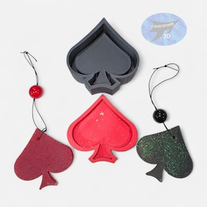 May include: A collection of spade-shaped ornaments in red, black, and green glitter, with a gray spade-shaped mold. Each ornament has a black string and a decorative bead. The image includes a logo that says "DUSTSTARR 3D".
