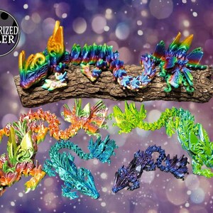 Könnte beinhalten: Eine Sammlung von sieben schillernden, handbemalten Drachenfiguren. Jeder Drache hat eine andere Farbe, darunter Grün, Blau, Lila, Orange und Gelb. Die Drachen sind auf einem Holzstamm angeordnet.