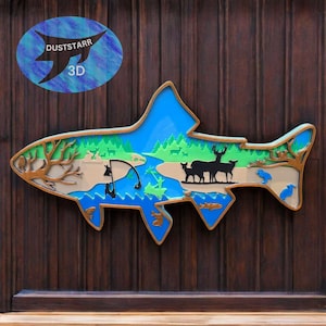 May include: A 3D wooden fish-shaped wall art piece with a layered design. The artwork features a blue sky, green trees, a river, and silhouettes of deer and birds. The artwork has the text "DUSTSTARR 3D" in a blue oval.