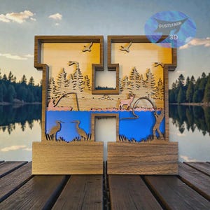 May include: Wooden letter "H" with a layered design depicting a lake scene. The scene includes trees, birds, and a person fishing. The colour palette features shades of brown, blue, and yellow. The base is a solid wooden block.