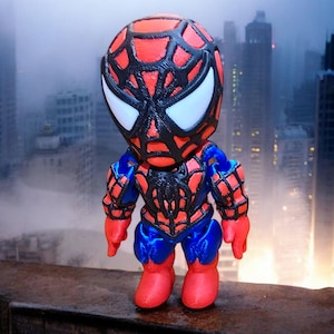 May include: A red and blue 3D printed figurine of Spider-Man standing on a brick surface. The figurine has a black web design on the suit and a white spider symbol on the chest.
