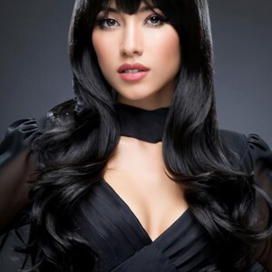 May include: A woman with long, black, wavy hair styled with a side part and bangs. She is wearing a black, low-cut, sleeveless dress.