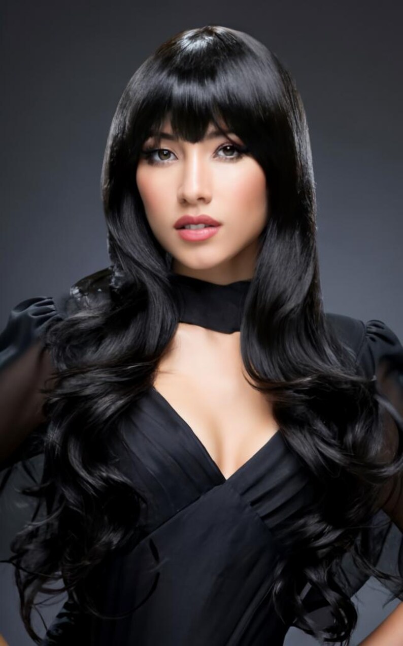 May include: A woman with long, black, wavy hair styled with a side part and bangs. She is wearing a black, low-cut, sleeveless dress.