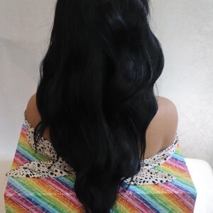 May include: A long, black wig with loose waves. The wig is styled in a way that creates volume and movement. The wig is displayed on a mannequin head with a colorful background.