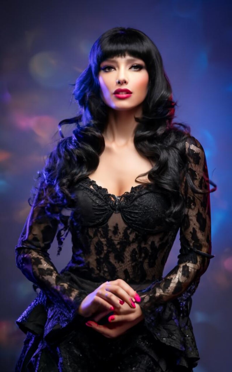 May include: A woman with long black hair and dark red lipstick wears a black lace dress with a low neckline. The dress has long sleeves and a ruffled skirt.