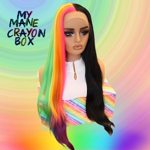 May include: A long, straight wig with half black hair and half rainbow coloured hair. The rainbow side is green, yellow, orange, pink, and purple. The wig is on a rainbow striped box with the text "MY MANE CRAYON BOX".