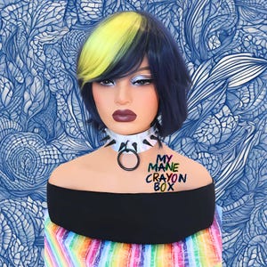 May include: A mannequin head with a two-tone wig, yellow and dark blue, and dramatic makeup. It wears a white choker with spikes and a black top. The text "MY MANE CRAYON BOX" is on the shoulder. The background is a blue pattern.
