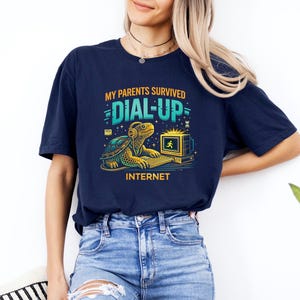 May include: Navy blue t-shirt with a graphic featuring a turtle wearing headphones and using a computer. The text reads "MY PARENTS SURVIVED DIAL-UP INTERNET". The design is in shades of teal, yellow, and gold.