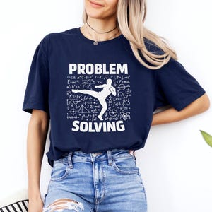 May include: Navy blue t-shirt with the words "PROBLEM SOLVING" in white, along with a graphic of a person kicking and mathematical equations. The shirt is a crew neck and is made of a soft material.