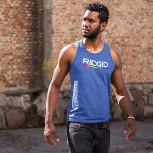 May include: Blue tank top with the word "RIDGID" in white and a rainbow stripe. The tank top is worn by a person in front of a brick wall. The person is wearing dark jeans and a bracelet.