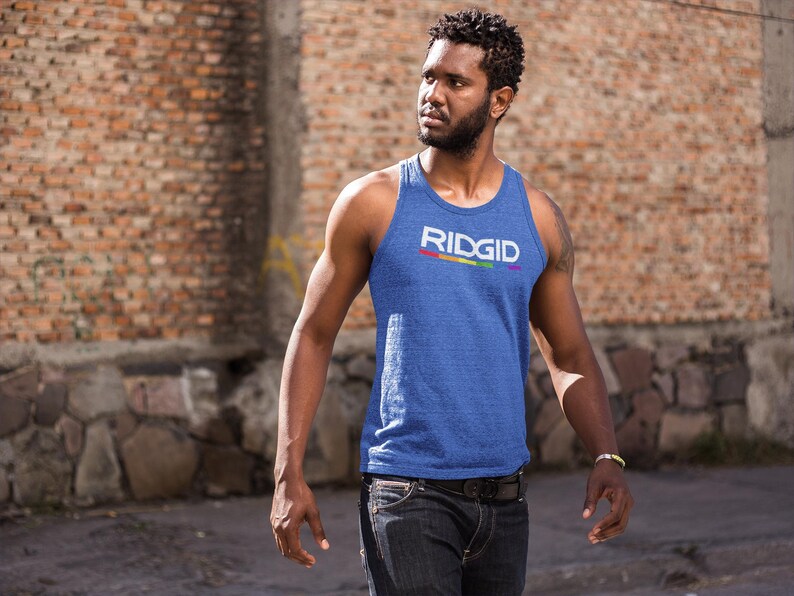 May include: Blue tank top with the word "RIDGID" in white and a rainbow stripe. The tank top is worn by a person in front of a brick wall. The person is wearing dark jeans and a bracelet.