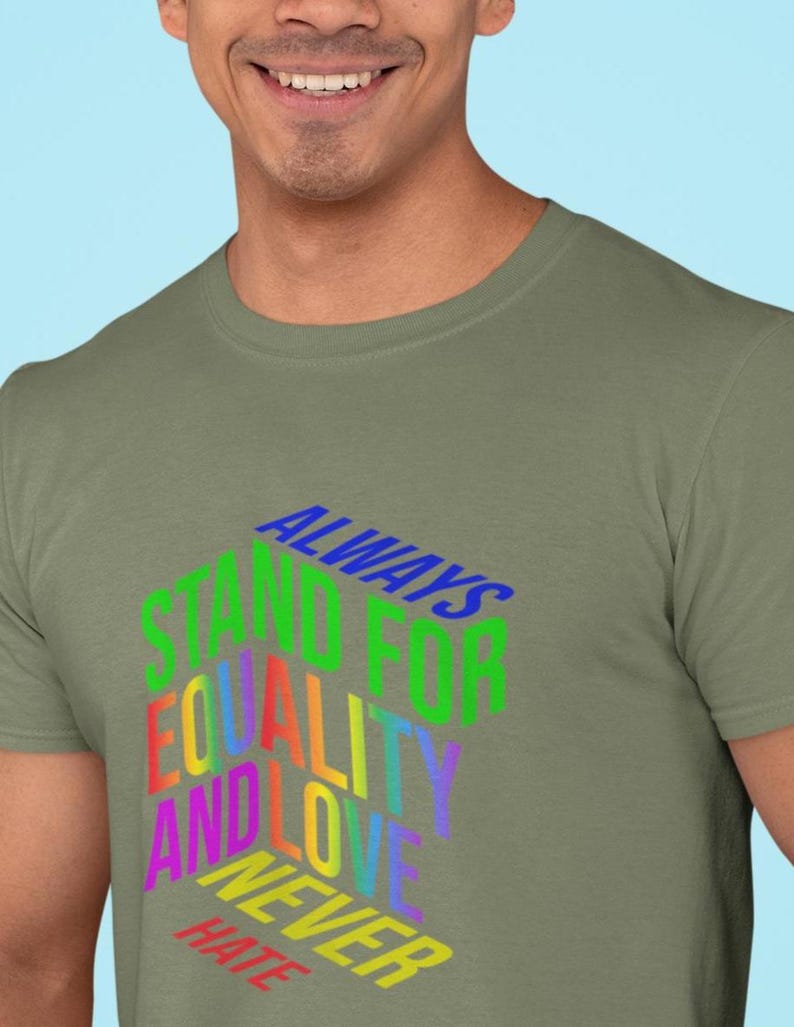 May include: Olive green t-shirt with the text "ALWAYS STAND FOR EQUALITY AND LOVE NEVER HATE" in a rainbow of colors. The text is in a 3D style, creating a bold and eye-catching design. The shirt is a casual wear item.