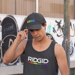 May include: A dark gray baseball cap with the word "BWINK" in rainbow colors. The person in the image is wearing a dark gray tank top with the word "RIDGID" in white and a rainbow-colored stripe.