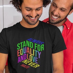 May include: Black t-shirt with the text "ALWAYS STAND FOR EQUALITY AND LOVE NEVER HATE" in a colorful, layered design. Two smiling people are visible in the image.