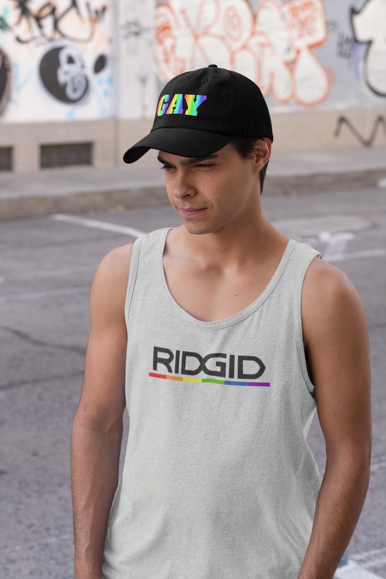 May include: Black baseball cap with the word "GAY" in rainbow colors. A light gray tank top with the word "RIDGID" in black and a rainbow stripe underneath.