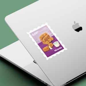 May include: A sticker featuring a stamp design with a purple background. The stamp depicts a stack of golden-brown tequeños, a small cup of white sauce, and the word "Miranda". The stamp is affixed to a laptop.