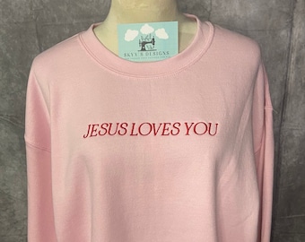 May include: A pink sweatshirt with the text "JESUS LOVES YOU" embroidered in red.