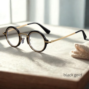 May include: Round eyeglasses with black rims and gold-coloured temples. The glasses have clear lenses. The text "black gold" is visible at the bottom of the image. The glasses are set against a neutral background.