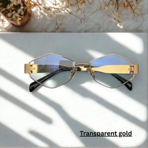 May include: Gold-framed sunglasses with a unique geometric shape and blue-tinted lenses. The text "Transparent gold" is printed at the bottom of the image. The sunglasses have a sleek, modern design.