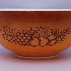 May include: A brown mixing bowl with a white rim and a brown and white fruit design. The bowl has a pour spout on each side.