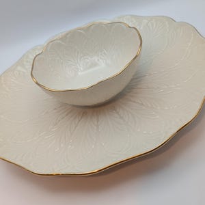 May include: A white ceramic serving dish with a gold rim and a matching bowl. The dish has a raised design of leaves and the bowl has a scalloped edge.