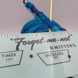 May include: A blue and green yarn ball with a knitting needle and a ruler that says "Forget-me-not Knitter's" with markings for "Times" and "Increase".