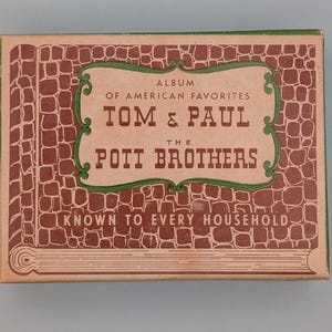 May include: A vintage album box with a brick-like pattern in brown and tan. The text reads "ALBUM OF AMERICAN FAVORITES TOM & PAUL THE POTT BROTHERS KNOWN TO EVERY HOUSEHOLD" in a decorative font, framed by a green border.