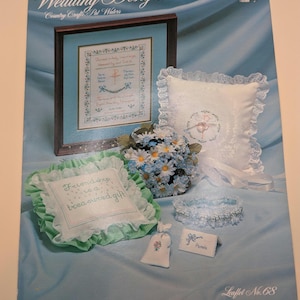 May include: A collection of wedding-themed cross-stitch designs. The image features a framed piece, decorative pillows, a bouquet of flowers, a garter, and a small gift bag. The text "Wedding Designs" and "Friendship is a treasured gift" are visible.